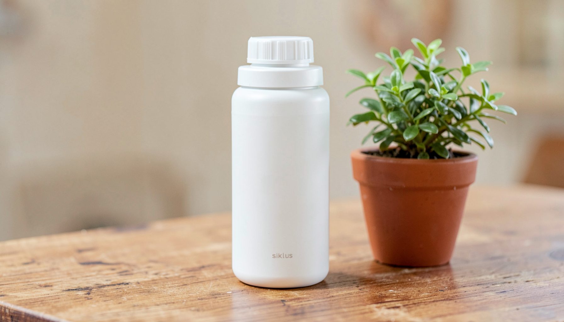 A reusable Siklus container with a simple screw cap, standing on a wooden table beside a small potted plant