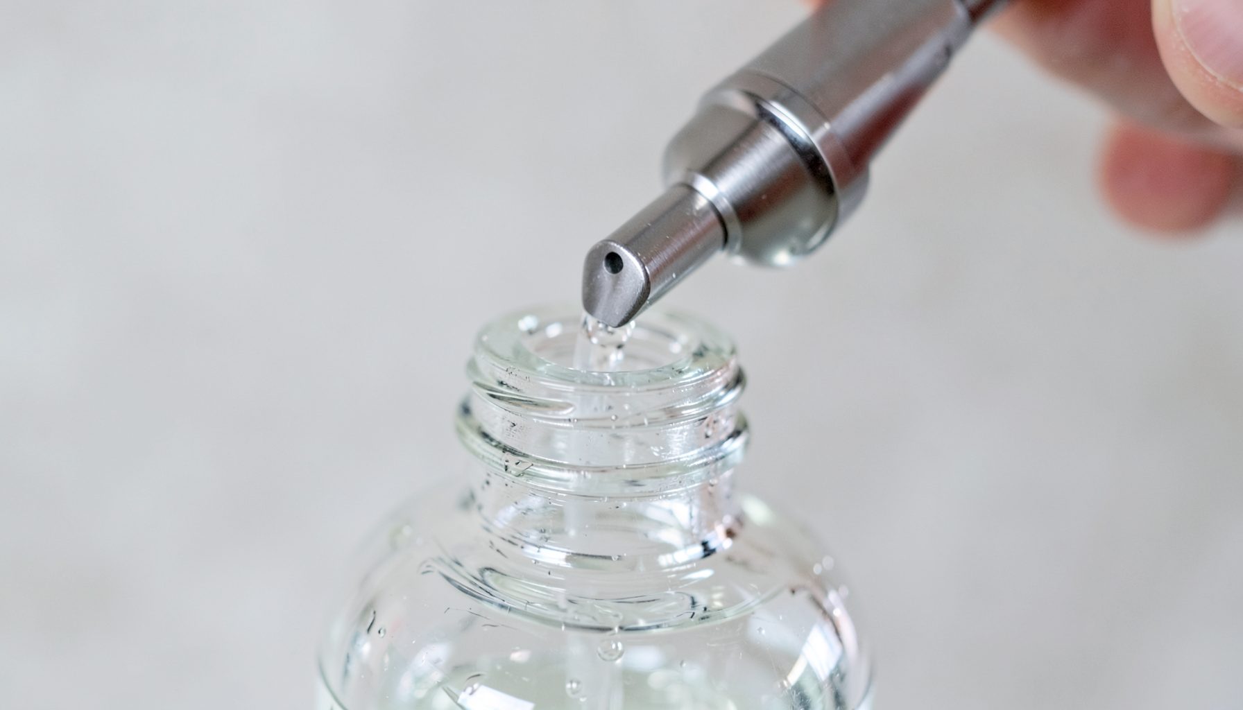 Close-up of liquid soap being dispensed into a clear reusable bottle from a stainless steel nozzle, clean and precise.
